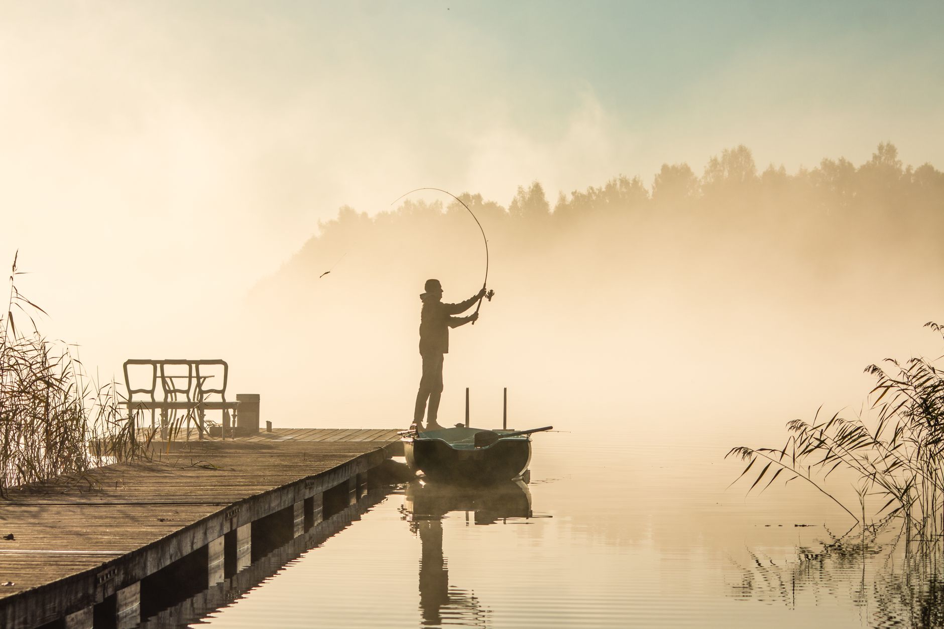 Einzelner Angler im Morgennebel beim Wurf, Spiegelung im Wasser